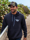 Man walking on beach wearing dark grey hoodie with a hang loose sign on the front