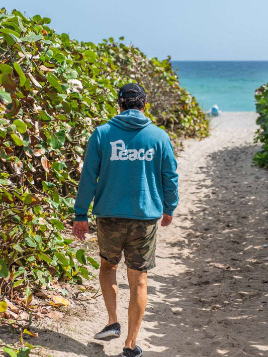 Man wearing blue hoodie with a the word 'Peace', walking on a beach