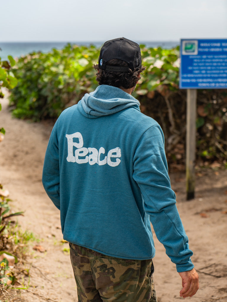 Man wearing blue hoodie with a the word 'Peace', walking on a beach