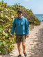 Man wearing blue hoodie with a peace sign, walking on a beach