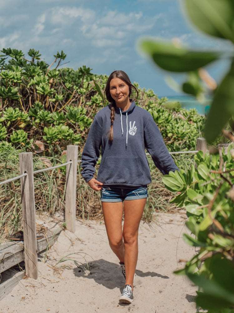 Man wearing grey hoodie with a hand signing peace, walking on a beach