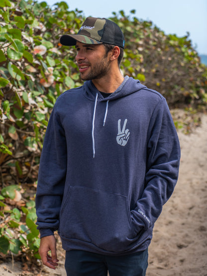 Man wearing navy hoodie with a hand signing peace, walking on a beach