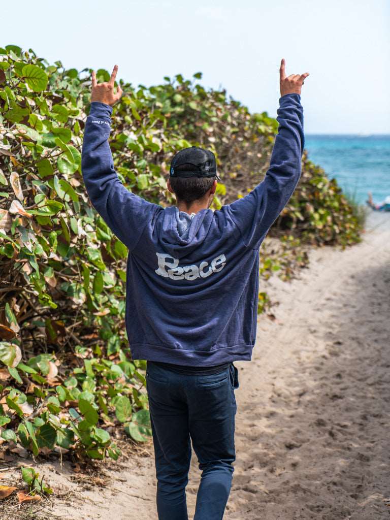 Man wearing navy hoodie with a the word 'Peace', walking on a beach