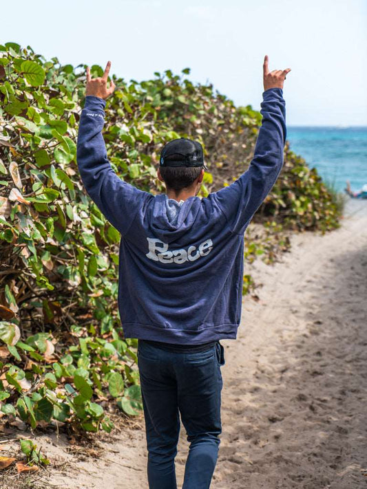 Man wearing navy hoodie with a the word 'Peace', walking on a beach