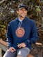 Man wearing navy hoodie with sun design, sitting on a wooden bench with trees in the background