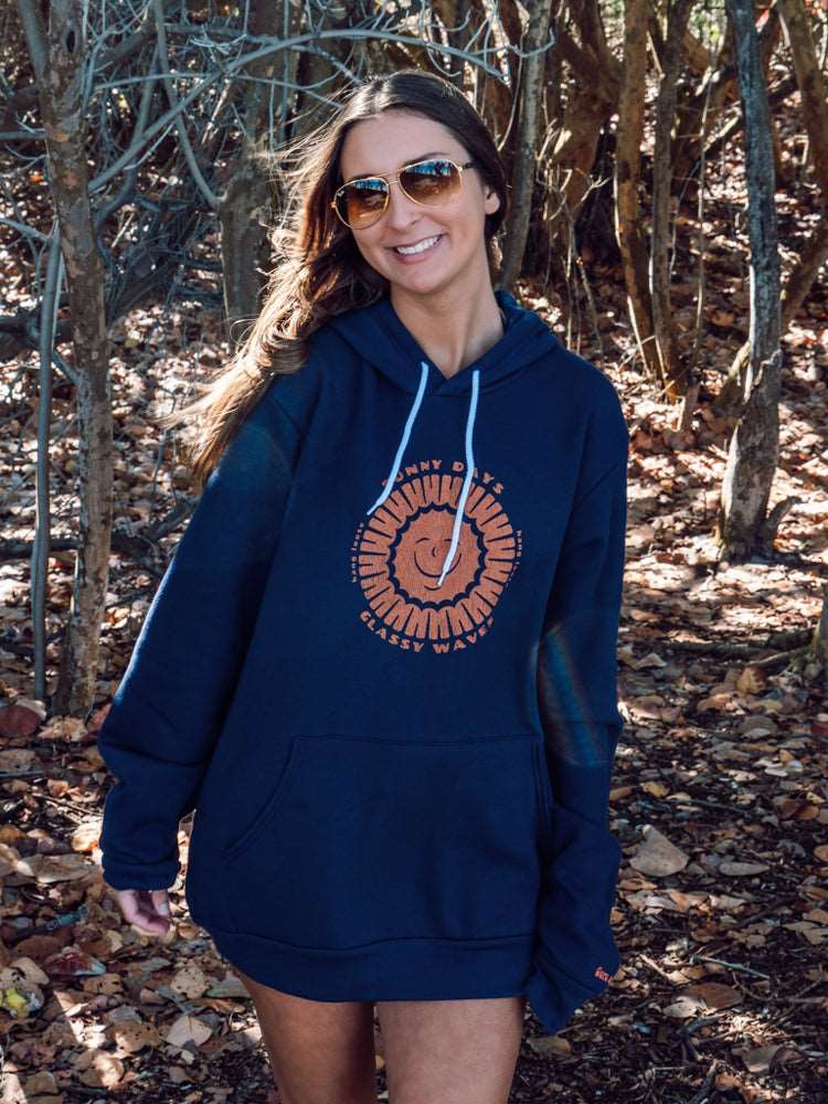 Woman wearing navy hoodie with sun design, with trees in the background