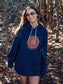 Woman wearing navy hoodie with sun design, with trees in the background