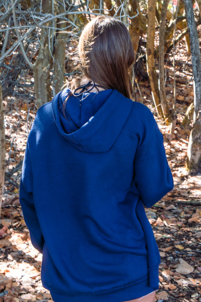 Woman wearing blue hoodie with trees in the background