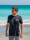 Man wearing a black t-shirt with 'Hang Loose' logo on the beach