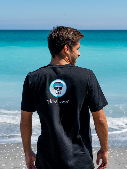 Man wearing a black t-shirt with 'Hang Loose' logo on the beach