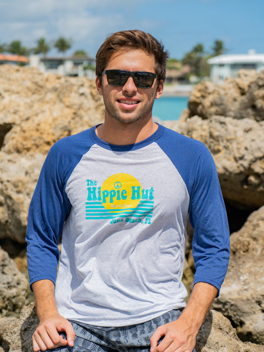 Man wearing a blue and white baseball shirt with a logo, sitting on rocks by a waterfront.