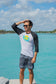 Man wearing a black and white baseball shirt with a logo, standing on a rock by water