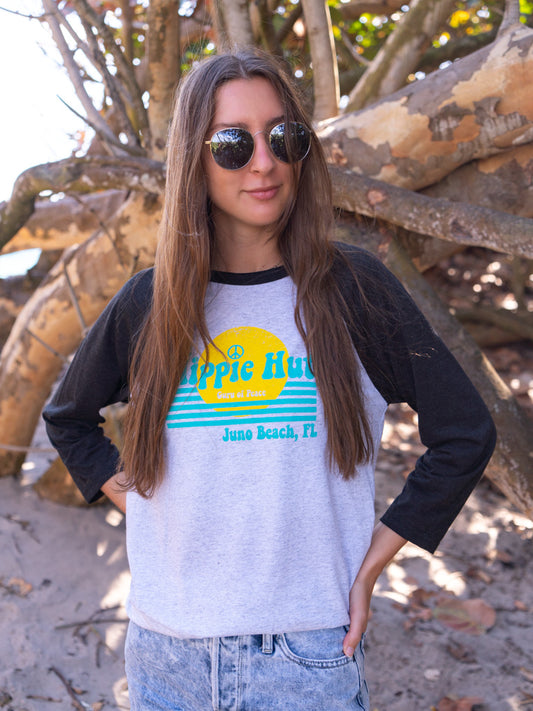 Woman wearing a black and white baseball shirt with a logo, standing by branches on a beach.