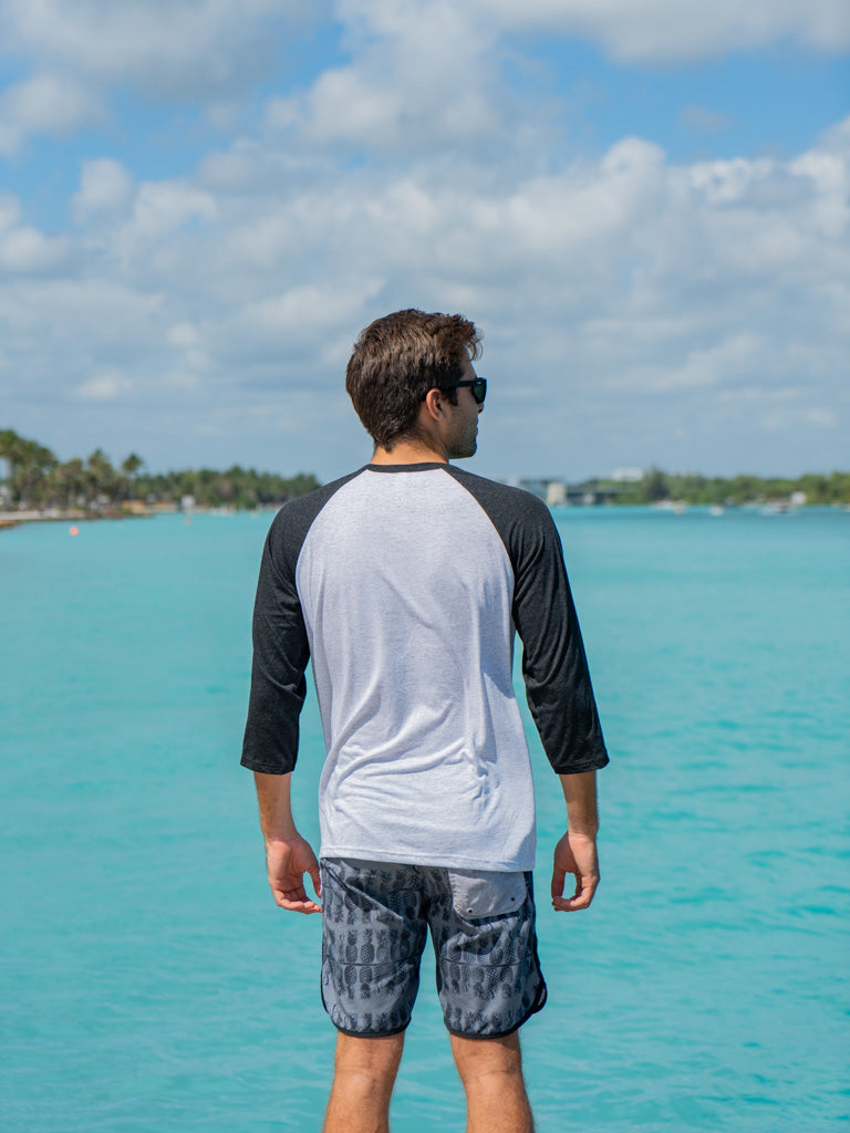 Man wearing a black and white baseball shirt, standing on a rock by water