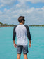 Man wearing a black and white baseball shirt, standing on a rock by water