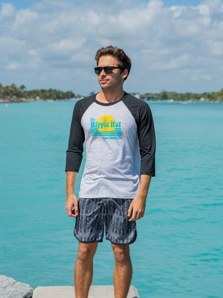Man wearing a black and white baseball shirt with a logo, standing on a rock by water