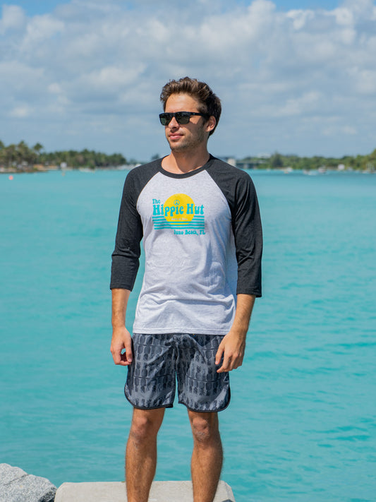 Man wearing a black and white baseball shirt with a logo, standing on a rock by water