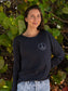 Woman standing with tree leaves in the background wearing a black long-sleeve shirt with a peace symbol.
