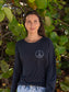 Woman standing by tree leaves wearing a black long-sleeve shirt with a peace symbol.