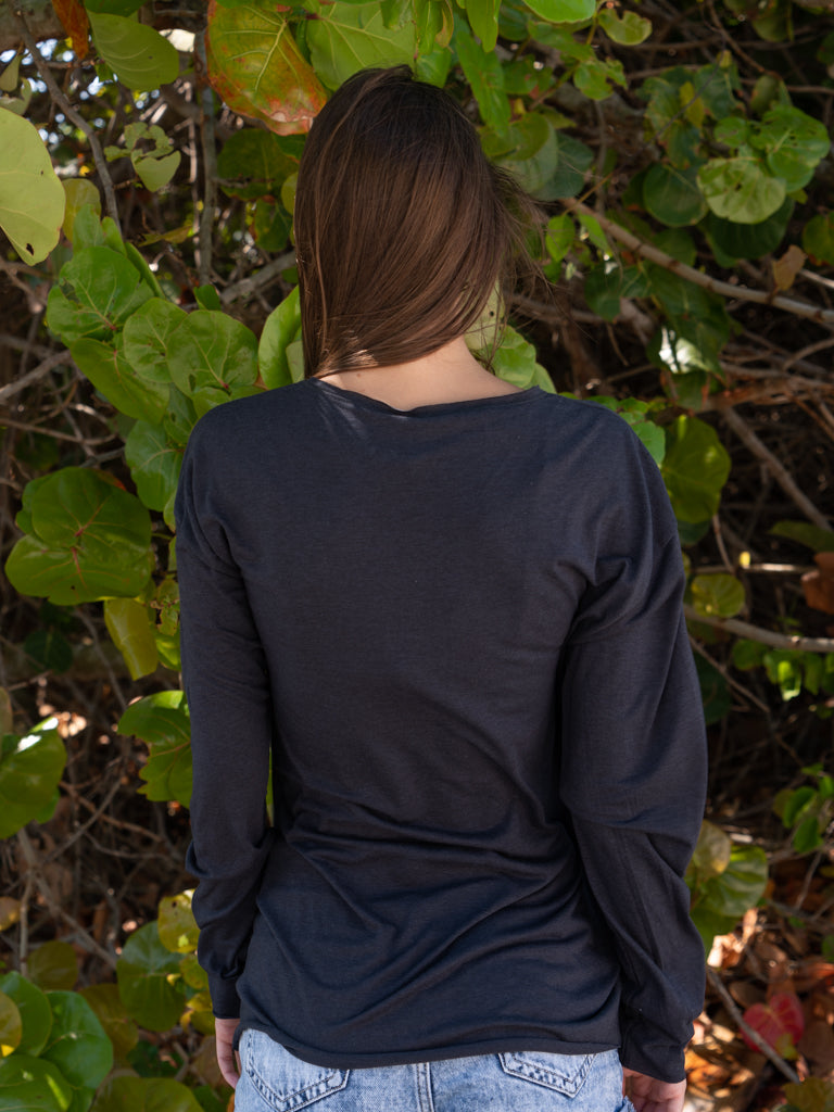 Woman standing with tree leaves in the background wearing a black long-sleeve shirt.