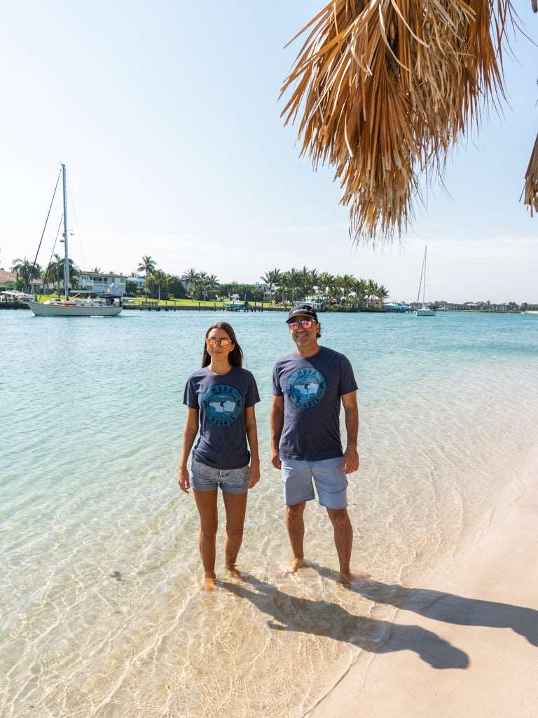Man and woman standing in the ocean wearing matching blue t-shirts with a design