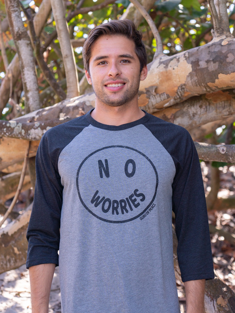 Man wearing a 'No Worries' shirt standing in front of wooden logs.