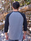 Man wearing a 'No Worries' shirt standing in front of wooden logs.