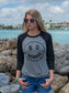 Woman wearing a 'No Worries' shirt standing in front of rocks and the ocean.