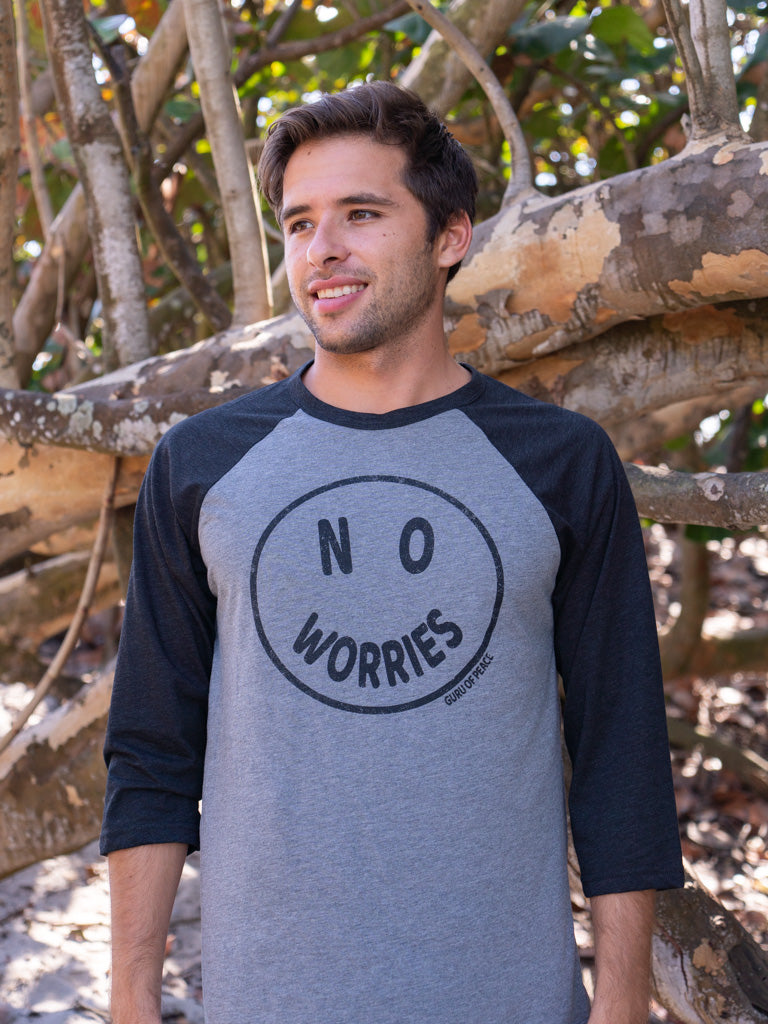 Man wearing a 'No Worries' shirt standing in front of wooden logs.