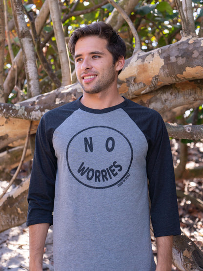 Man wearing a 'No Worries' shirt standing in front of wooden logs.