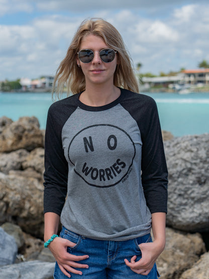 Woman wearing a 'No Worries' shirt standing in front of rocks and the ocean