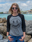 Woman wearing a 'No Worries' shirt standing in front of rocks and the ocean