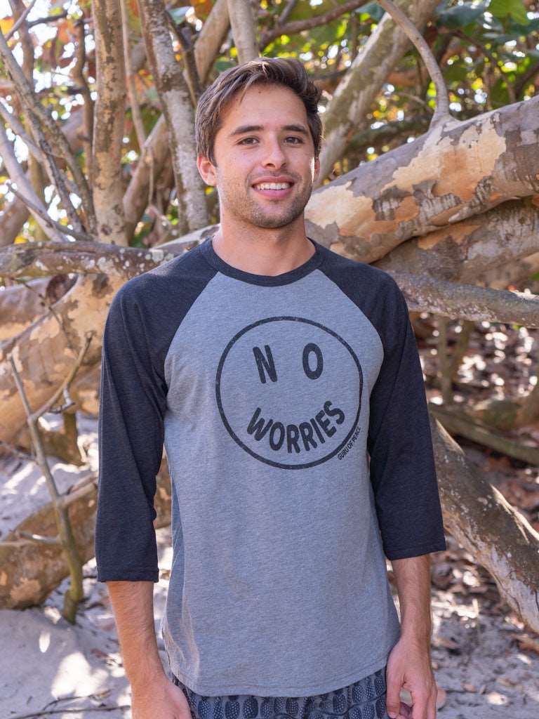 Man wearing a 'No Worries' shirt standing in front of wooden logs.