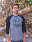 Man wearing a 'No Worries' shirt standing in front of wooden logs.
