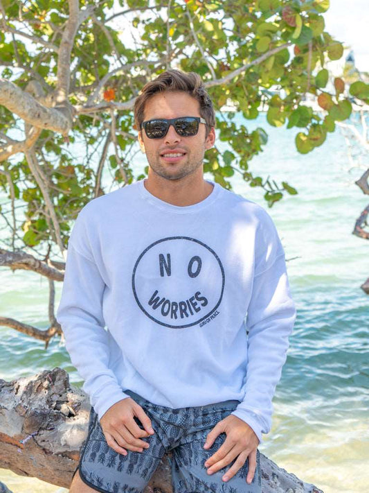 Man wearing a 'No Worries' sweatshirt by a body of water with trees in the background