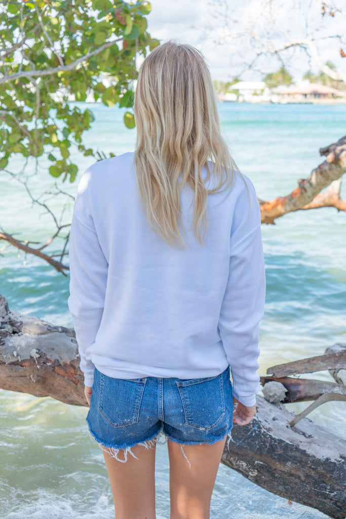 Woman wearing a white sweatshirt by a body of water with trees in the background