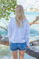 Woman wearing a white sweatshirt by a body of water with trees in the background