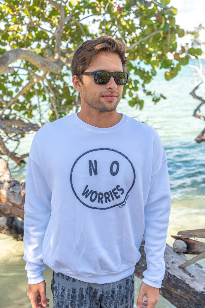 Man wearing a white sweatshirt with the words 'No Worries' by a body of water with trees in the background