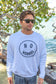 Man wearing a white sweatshirt with the words 'No Worries' by a body of water with trees in the background