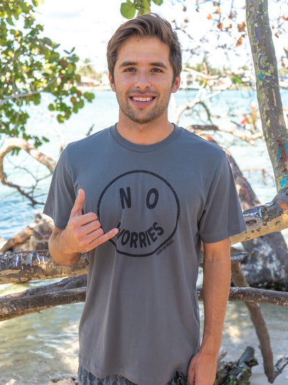 Man wearing a gray t-shirt with 'No Worries' graphic, standing by a body of water.