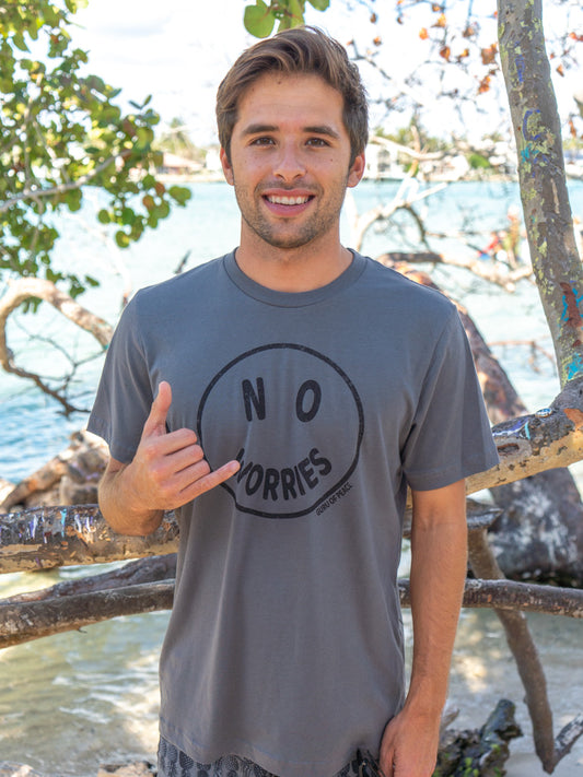 Man wearing a gray t-shirt with 'No Worries' graphic, standing by a body of water.