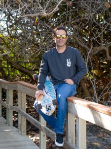 Man sitting on a wooden railing with sunglasses and a blue sweatshirt