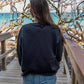 Woman standing on a wooden boardwalk with sunglasses and a black sweatshirt