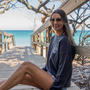 Woman sitting on a wooden boardwalk with sunglasses and a blue sweatshirt