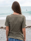Woman standing on a beach, wearing a green t-shirt, looking out at the ocean
