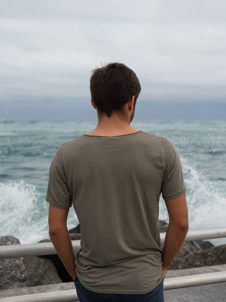 Man standing on a bridge, wearing a green t-shirt, looking out at the ocean