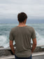 Man standing on a bridge, wearing a green t-shirt, looking out at the ocean