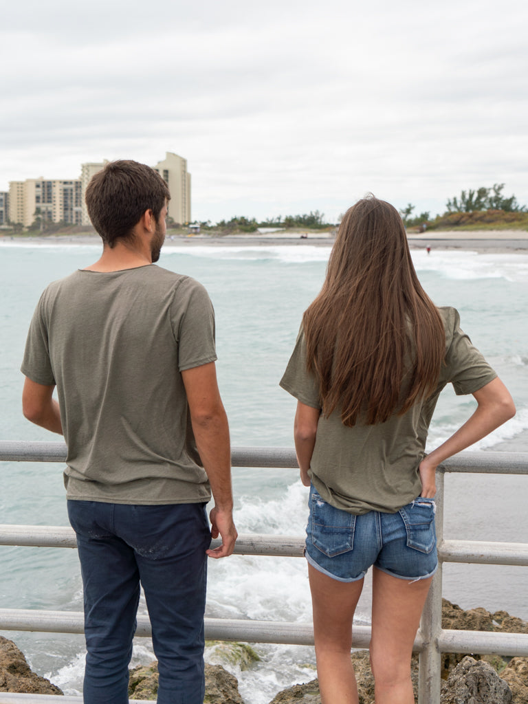 Man and woman standing on a bridge with the ocean in the background, wearing matching green t-shirts