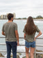 Man and woman standing on a bridge with the ocean in the background, wearing matching green t-shirts