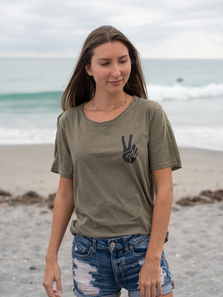 Woman walking on a beach, wearing a green t-shirt with a logo.